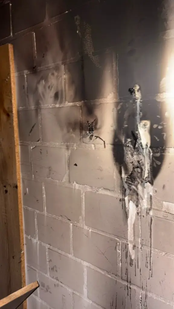 Brandstelle im Keller: verrußtes Mauerwerk und geschmolzener, heruntergelaufener Kunststoff an der Wand